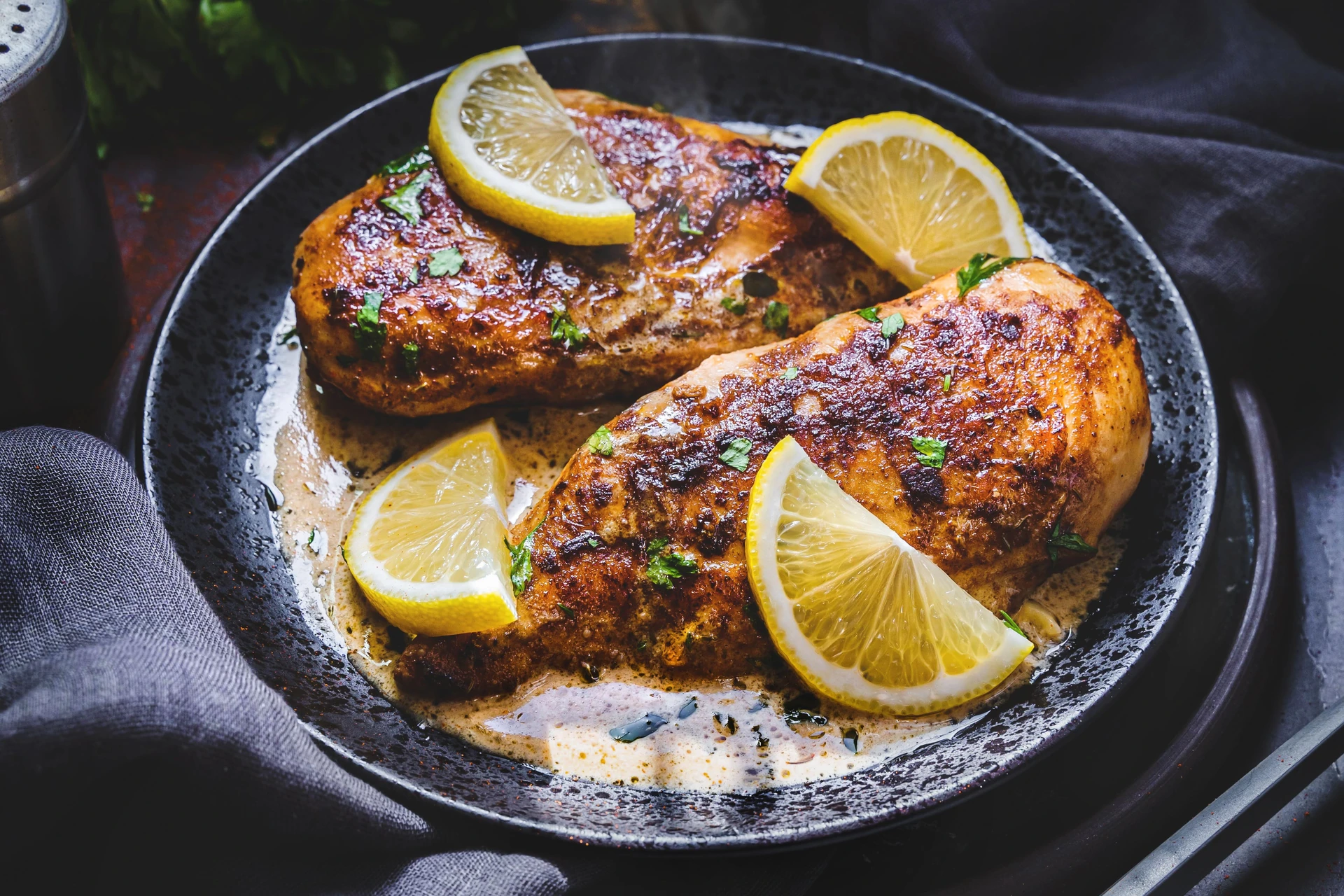 Seasoned chicken with lemon on a dark plate
